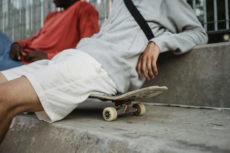 a man sitting on top of a skateboard next to another man, trending on pexels, hyperrealism, passed out, wearing a grey hooded sweatshirt, off - white collection, 15081959 21121991 01012000 4k