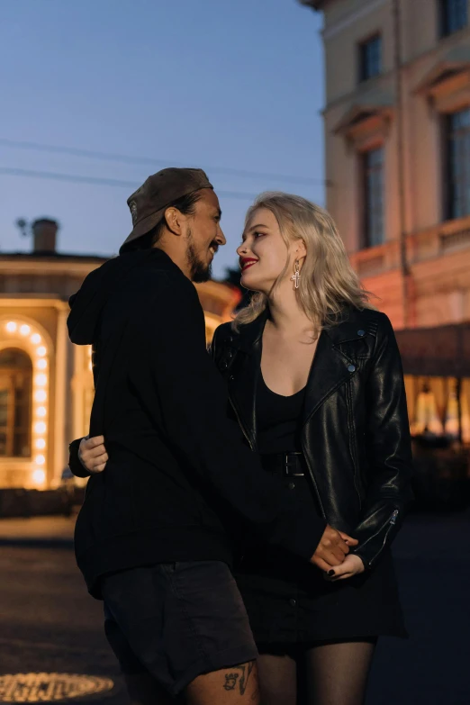 a man and woman standing next to each other in front of a building, by Jaakko Mattila, pexels contest winner, antipodeans, city lights in the background, smiling at each other, black, attractive man