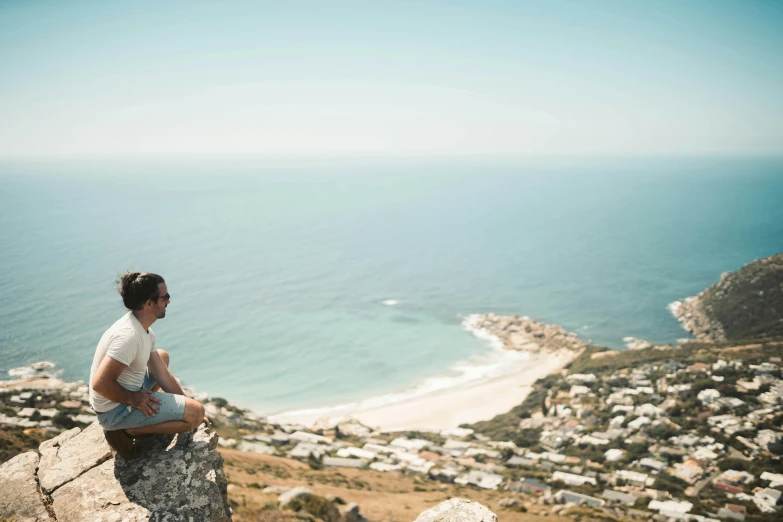 a woman sitting on a rock overlooking the ocean, by Daniel Lieske, pexels contest winner, happening, cape, view over city, on a sunny day, person in foreground