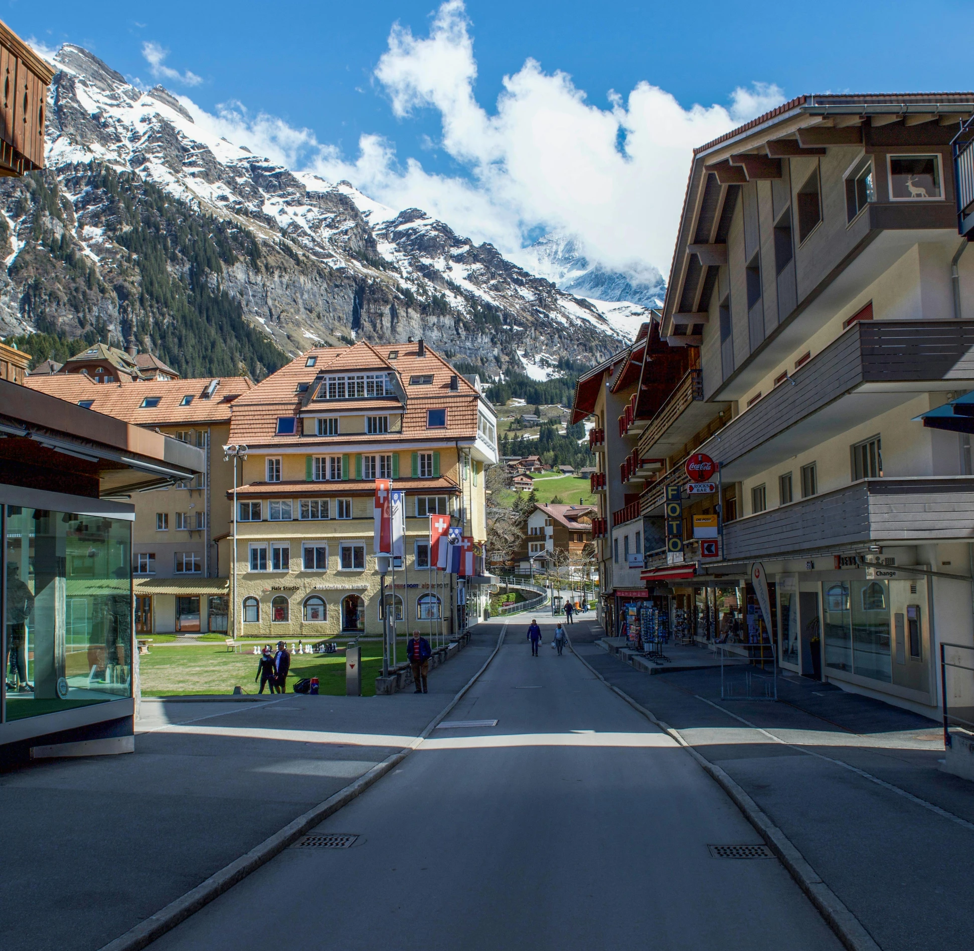 a city street with buildings and mountains in the background, inspired by Karl Stauffer-Bern, pexels contest winner, lauterbrunnen valley, square, ground level shot, modern street