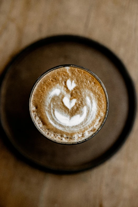 a cup of coffee sitting on top of a wooden table, heart-shaped face, thumbnail, subtle detailing, latte art