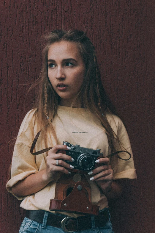 a girl holding a camera in front of a red wall, inspired by Elsa Bleda, pexels contest winner, realism, wearing yellow croptop, portrait of white teenage girl, low quality grainy, woman with braided brown hair