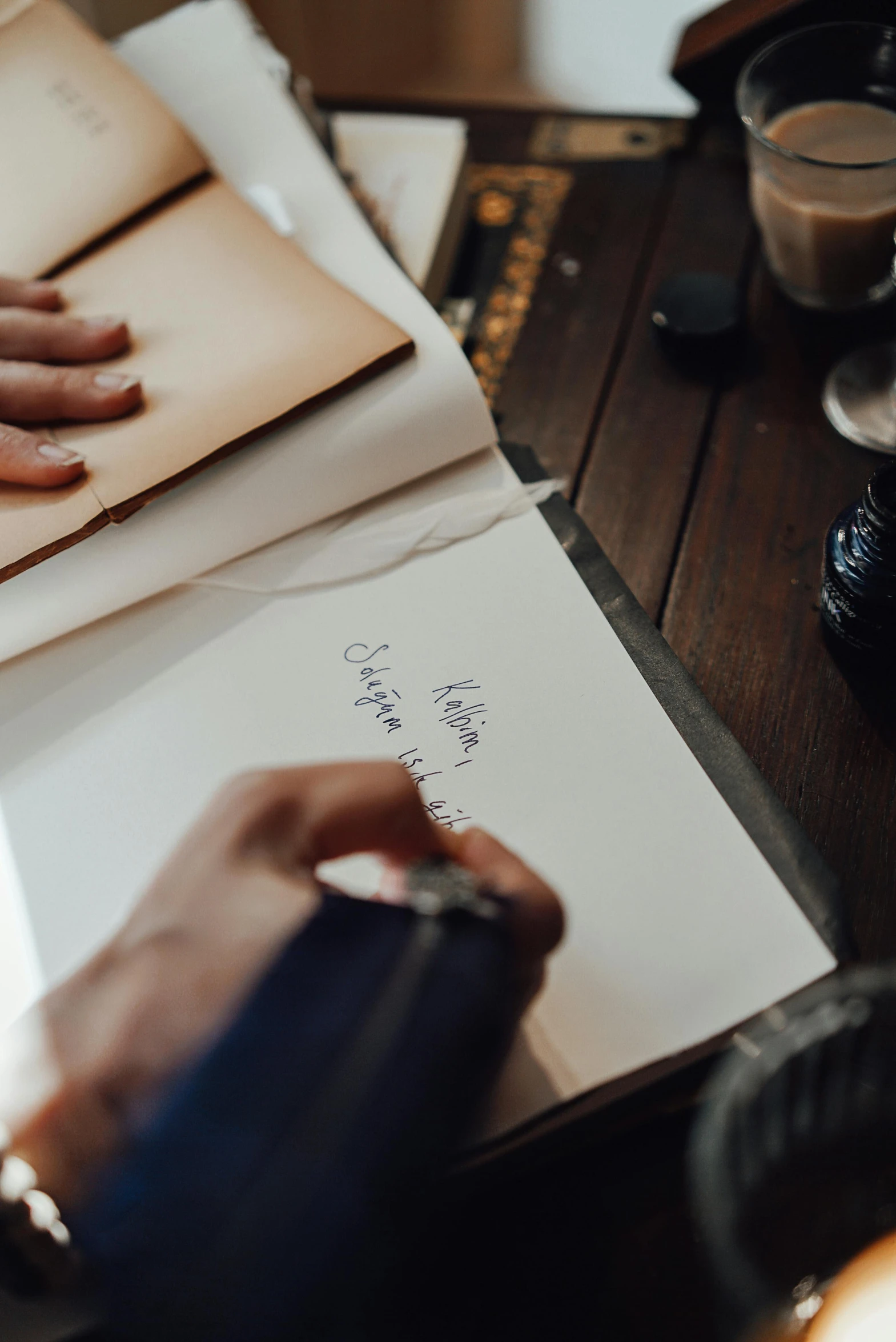 a person sitting at a table writing on a piece of paper, an album cover, by Julia Pishtar, unsplash contest winner, private press, estrange calligraphy, spell book, wedding, brown