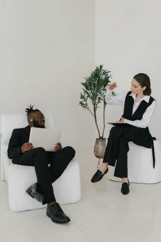 a woman sitting in a chair next to a man on a laptop, pexels contest winner, in white room, conversation pit, black suit, person made of tree