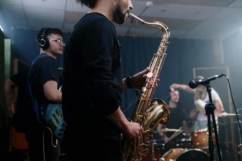 a man that is playing a saxophone in a room, studio kai, thumbnail, group photo, in the background