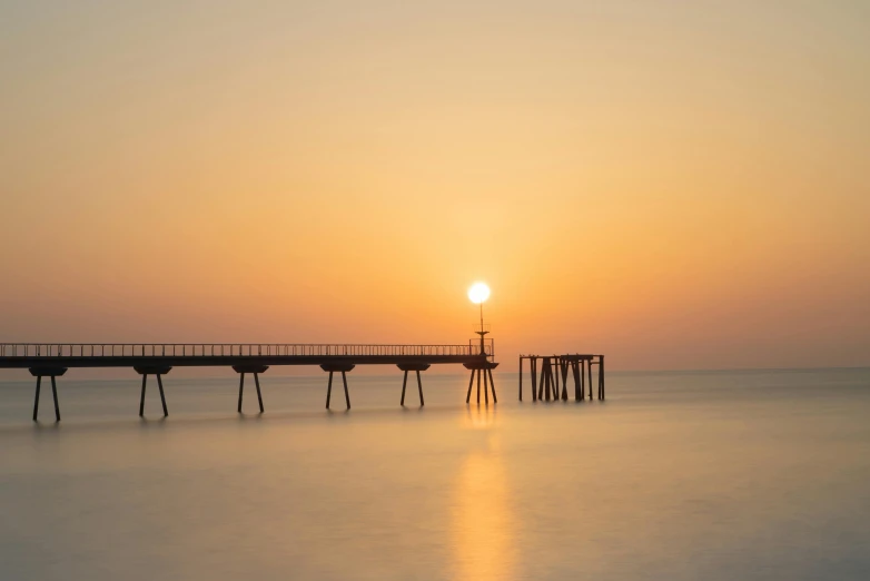 a pier in the middle of the ocean at sunset, by Eglon van der Neer, pexels contest winner, light haze, cyprus, at sunrise in springtime, brown