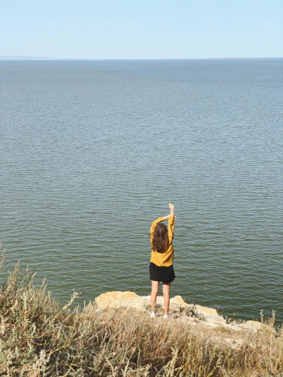 a woman standing on top of a cliff flying a kite, gazing at the water, near lake baikal, dafne keen, 2019 trending photo