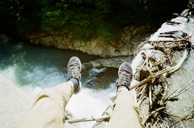 a person sitting on a log over a river, pexels contest winner, head straight down, on a birdge, sneaker photo, kodak portra