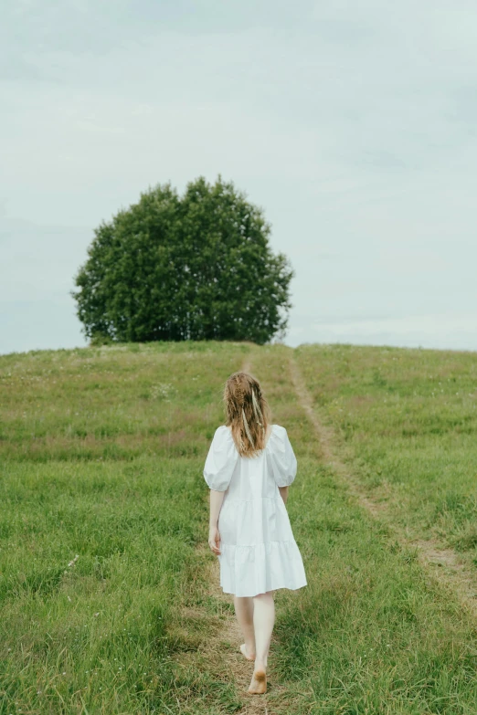 a woman in a white dress walking in a field, trees in the grassy hills, tiny person watching, swedish countryside, press shot