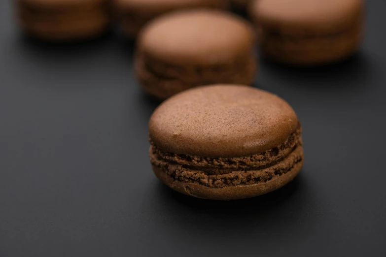 a group of chocolate macarons sitting on top of a table, a macro photograph, trending on pexels, detailed product image, dark-skinned, 15081959 21121991 01012000 4k, brown fringe