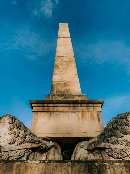 a statue of two lions with a obelisk in the background, by Joseph Henderson, pexels contest winner, neoclassicism, wide angel shot from below, sunken square, ossuary, blue sky