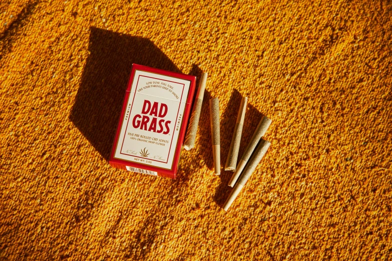 a pack of cigarettes sitting on top of a carpet, red grass, dad, the grass, detailed product image