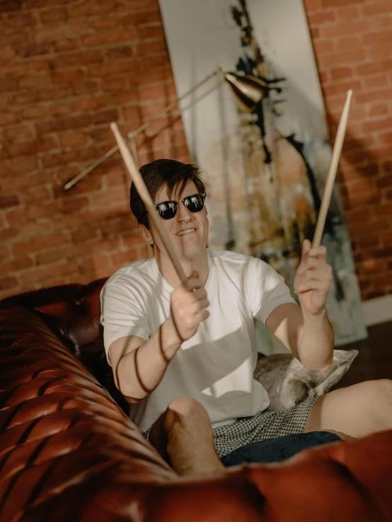 a man sitting on a couch holding a pair of drums, inspired by Dicky Doyle, pexels contest winner, discord profile picture, shades, lachlan bailey, he wears an eyepatch