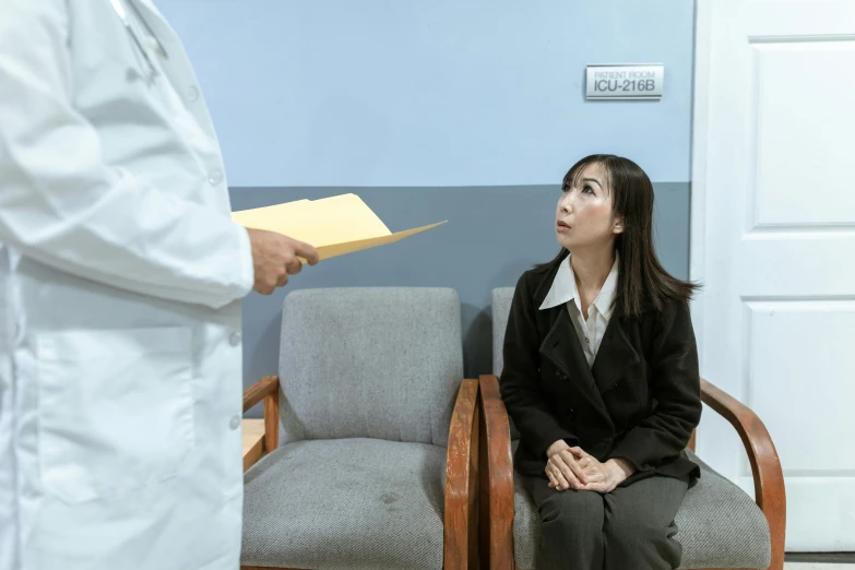 a woman sitting in a chair in a doctor's office, a colorized photo, pexels contest winner, shin hanga, scolding, background image, thumbnail, japanese