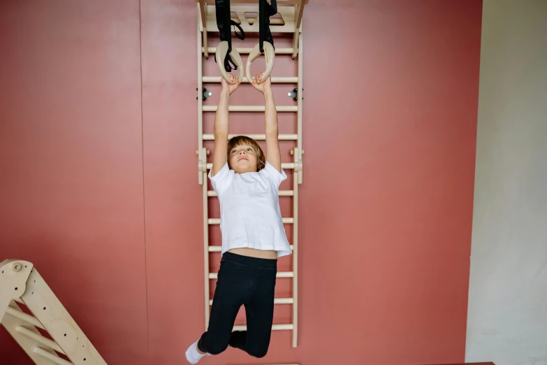 a little boy that is standing on a ladder, by Nina Hamnett, dim dingy gym, stretching to walls, square, birch
