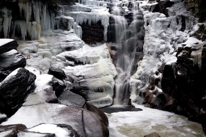 a waterfall surrounded by snow and ice covered rocks, pexels contest winner, new hampshire, thumbnail, black, sandfalls