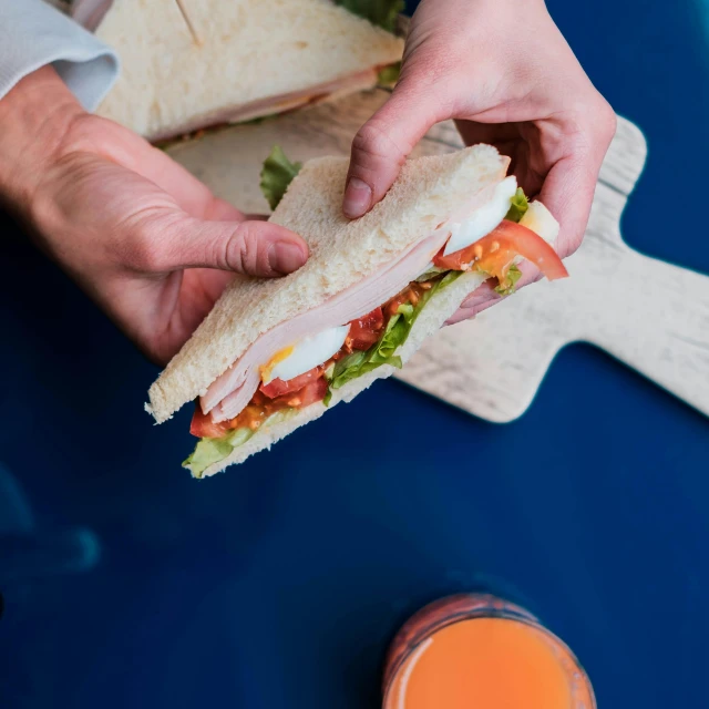 a person holding a sandwich on a cutting board, by Julia Pishtar, pexels contest winner, orange and blue color scheme, high class, american canteen, thumbnail