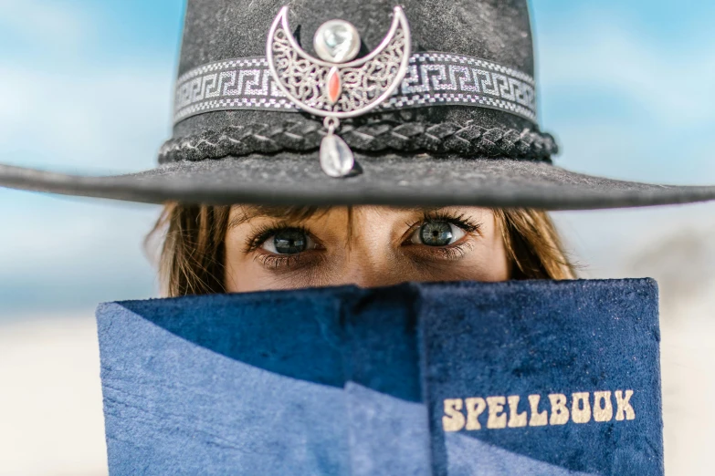 a woman wearing a hat and holding a spellbook, an album cover, by Greg Spalenka, unsplash contest winner, lowbrow, close - up shot of eyes, photo from a spectator, blue fedora, spellbreak