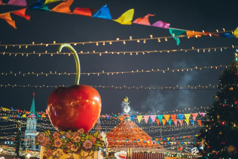 a large red apple sitting on top of a christmas tree, by Julia Pishtar, maximalism, with street food stalls, big top circus tent, glowing temple in the distance, fairy lights