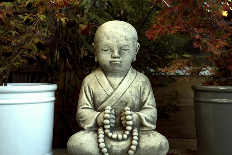 a buddha statue sitting in front of a potted plant, little boy wearing nun outfit, stone sculpture, grey, shodan