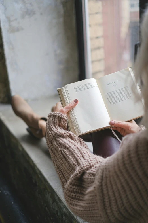 a woman sitting on a window sill reading a book, pexels contest winner, wearing casual sweater, open books, subtle detailing, dusty library