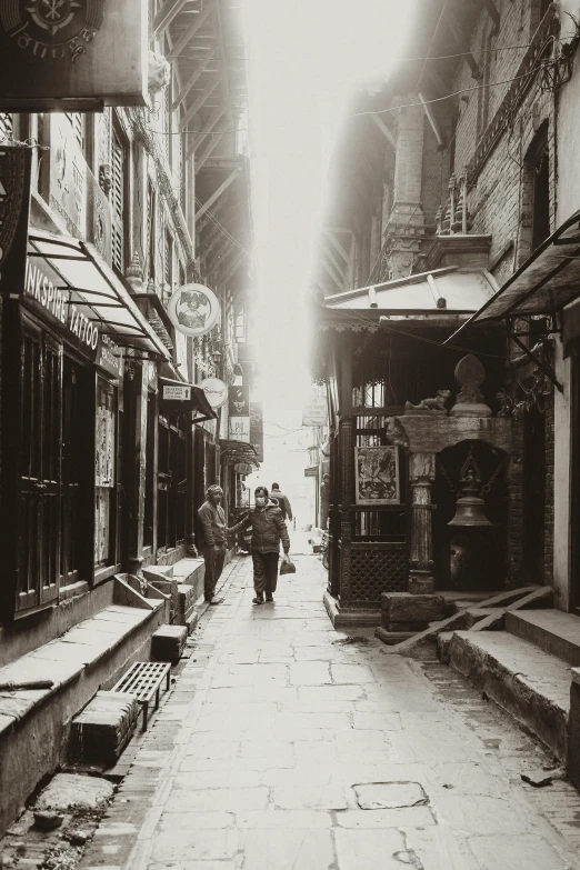 a couple of people that are walking down a street, a black and white photo, art nouveau, nepal, old shops, shafts of light, location [ chicago ( alley ) ]