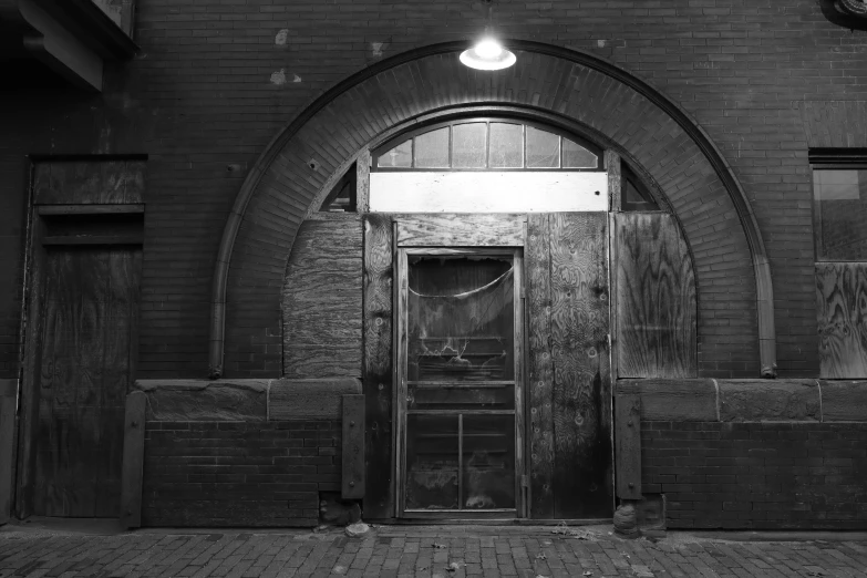 a black and white photo of a doorway in a building, by Andrew Domachowski, brick building, market, back arched, boarded up