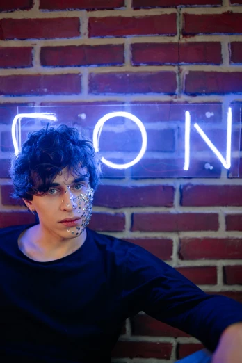 a young man sitting in front of a neon sign, by Siona Shimshi, trending on pexels, serial art, with haunted eyes and curly hair, andy milonakis, xenon, confetti