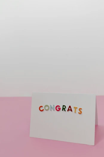 a card with the word congrats on it, by Nicolette Macnamara, pexels contest winner, letterism, rainbow accents, indoor picture, shot in canon, 3/4 front view