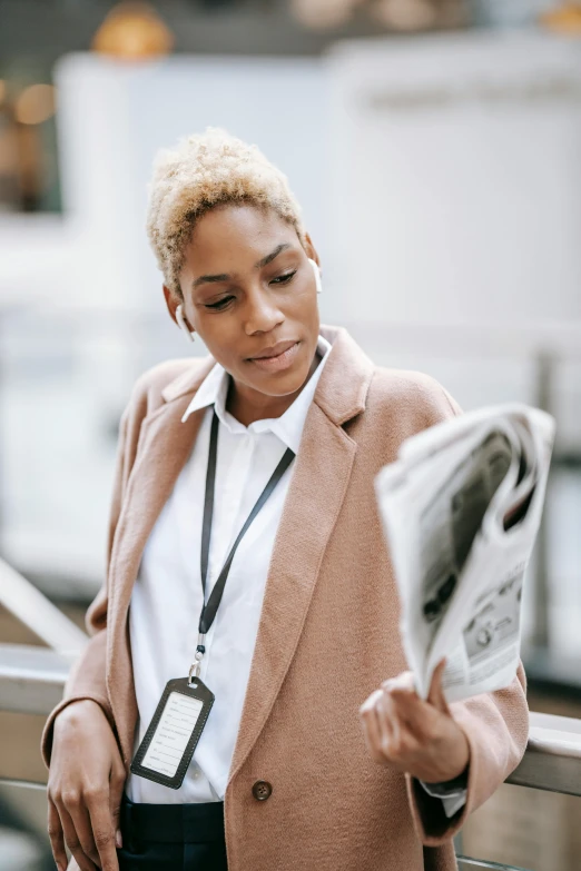 a woman reading a newspaper on an escalator, trending on pexels, private press, light brown coat, wearing lab coat and a blouse, african american young woman, blonde women