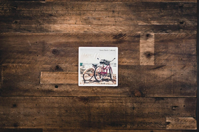 a book sitting on top of a wooden table, an album cover, by Daniel Gelon, unsplash, bicycles, square sticker, ad image