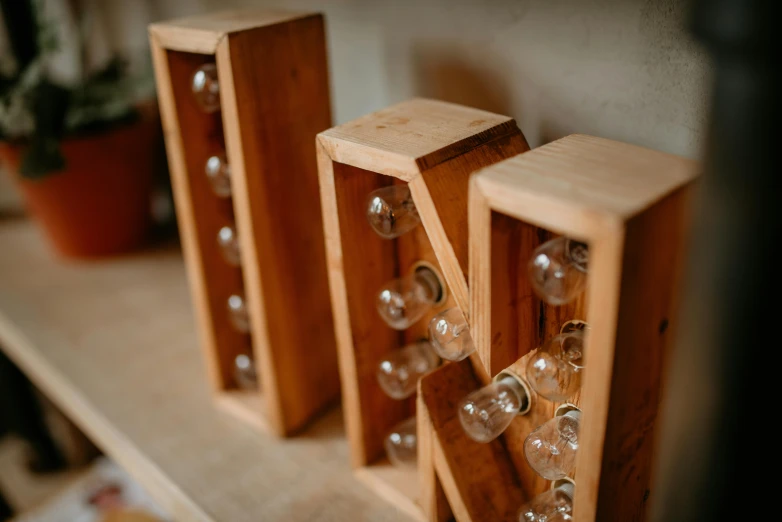 three wooden wine bottles on a shelf next to a potted plant, unsplash, letterism, small nixie tubes, led lamps, wooden crates, bottom - view