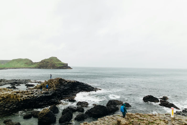 a couple of people standing on top of a rocky beach, pillhead, rope bridge, hazy water, wide views