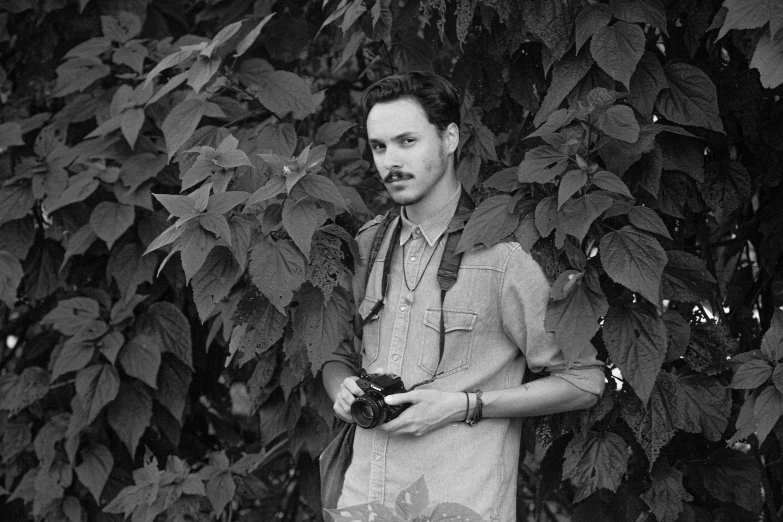 a black and white photo of a man holding a camera, by Maurycy Gottlieb, clothed in vines, with mustache, matt rhodes, 1987 photograph