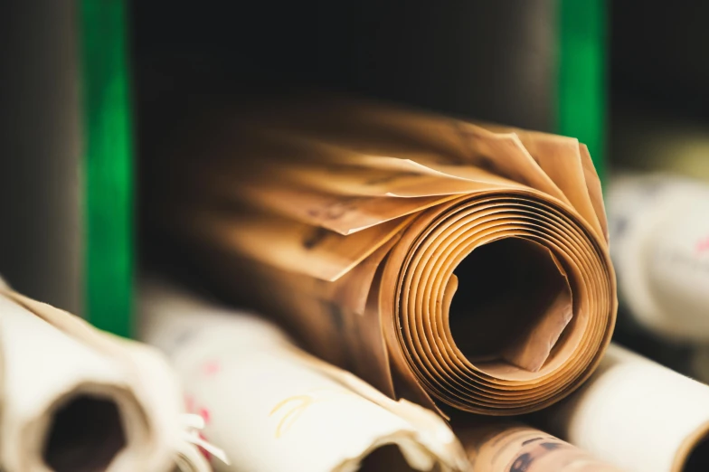 a roll of paper sitting on top of a table, unsplash, arts and crafts movement, copper and emerald, high quality printing, brown paper, multiple stories