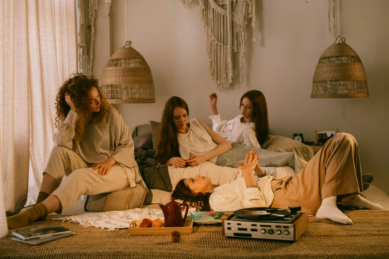 a group of people sitting on top of a bed, inspired by Elsa Bleda, trending on pexels, aestheticism, 7 0 s living room, listening to music, 3 young and beautiful women, sitting on a mocha-colored table