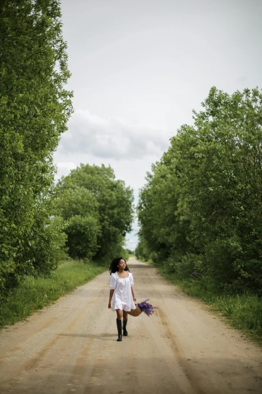 a woman walking down a dirt road with a basket of flowers, inspired by Isaac Levitan, pexels contest winner, trees around, minn, pretty girl, quebec