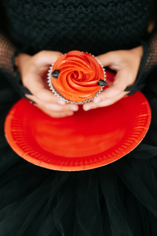 a woman in a black dress holding a red cupcake, pexels, orange color scheme, on a plate, rosette, gothic