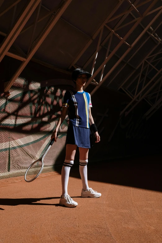 a man standing on a tennis court holding a racquet, an album cover, inspired by Hans Mertens, unsplash, fashion shoot 8k, costume with blue accents, evening sun, ( ( theatrical ) )