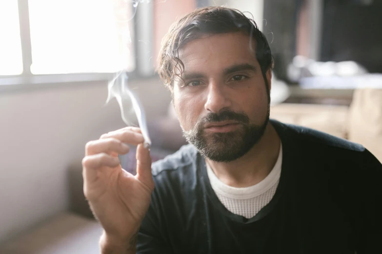 a man sitting at a table with a cigarette in his hand, a portrait, inspired by Pablo Munoz Gomez, pexels contest winner, renaissance, pot leaf, zachary quinto, holding it out to the camera, smoky laboratory