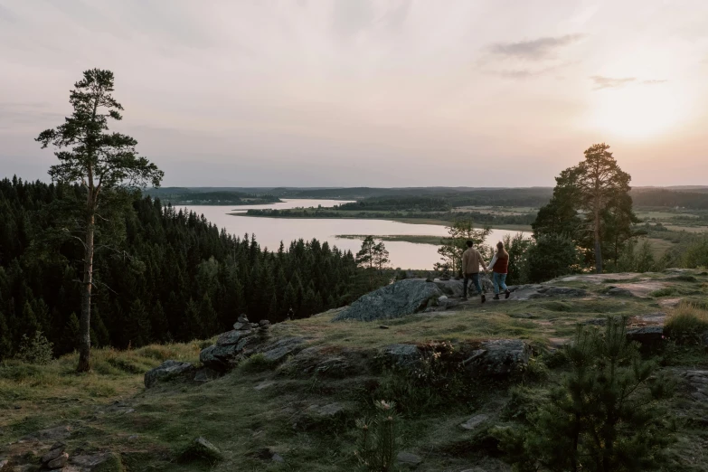 a group of people standing on top of a lush green hillside, by Anton Lehmden, forest with lake, pink golden hour, archipelago, grey