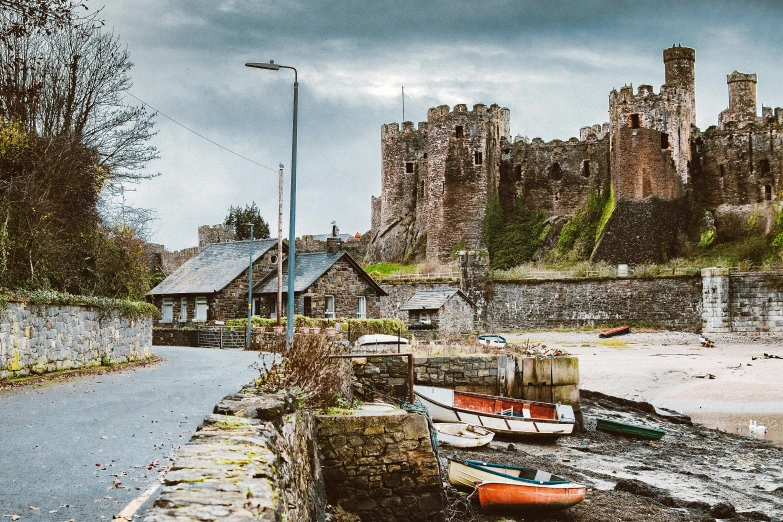 a couple of boats sitting on the side of a road, by Gwilym Prichard, pexels contest winner, arts and crafts movement, giant castle walls, mossy buildings, thumbnail, red castle in background