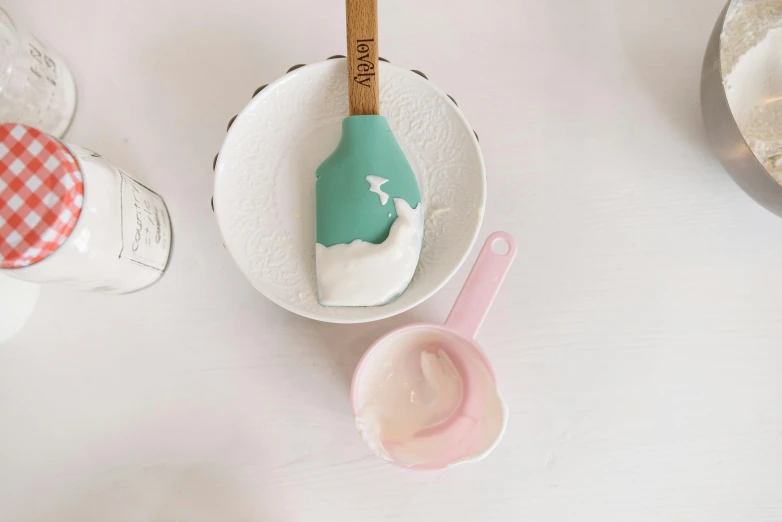 a green spatula sitting on top of a white plate, teal and pink, silicone skin, sea of milk, on a wooden table