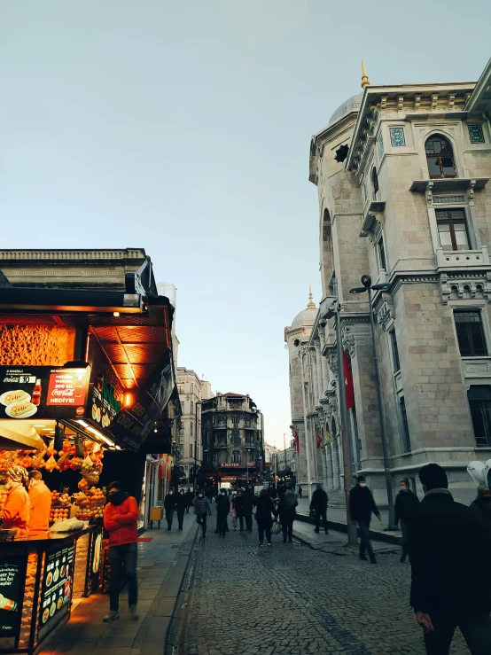 a group of people walking down a street next to tall buildings, art nouveau, istanbul, profile image, food stalls, warmly lit