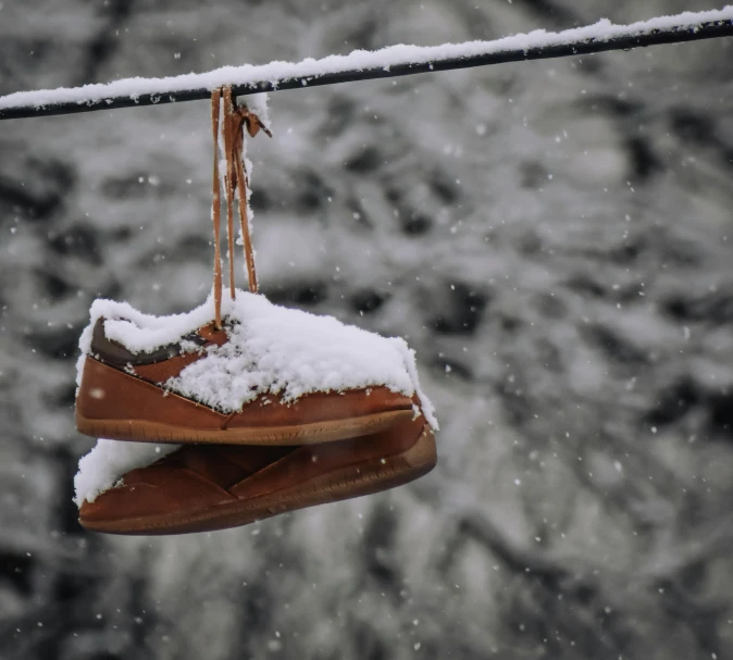 a pair of shoes hanging from a wire in the snow, pexels contest winner, brown, low key, # glazersout, slippers