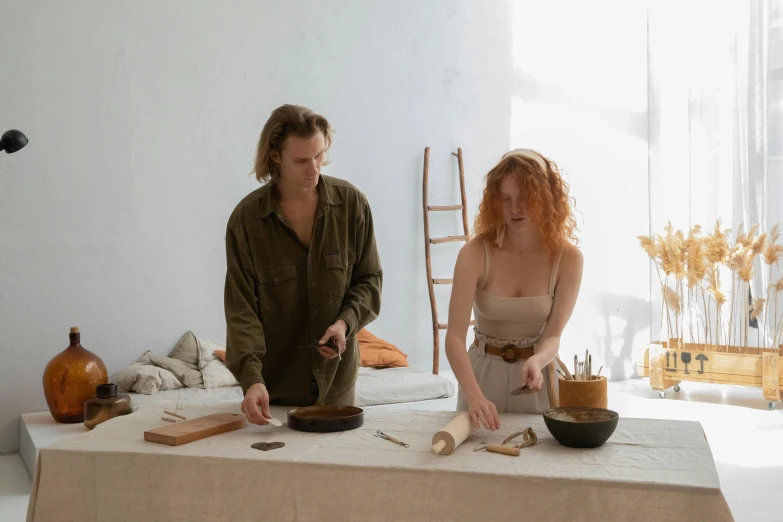 a man and a woman preparing food on a table, by Emma Andijewska, pexels contest winner, renaissance, in a white boho style studio, clay material, tools, ( redhead