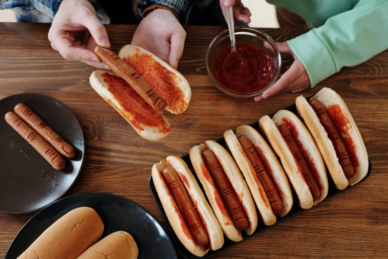 a table topped with lots of hot dogs covered in ketchup, by Julia Pishtar, sleek hands, thumbnail, sichuan, bread