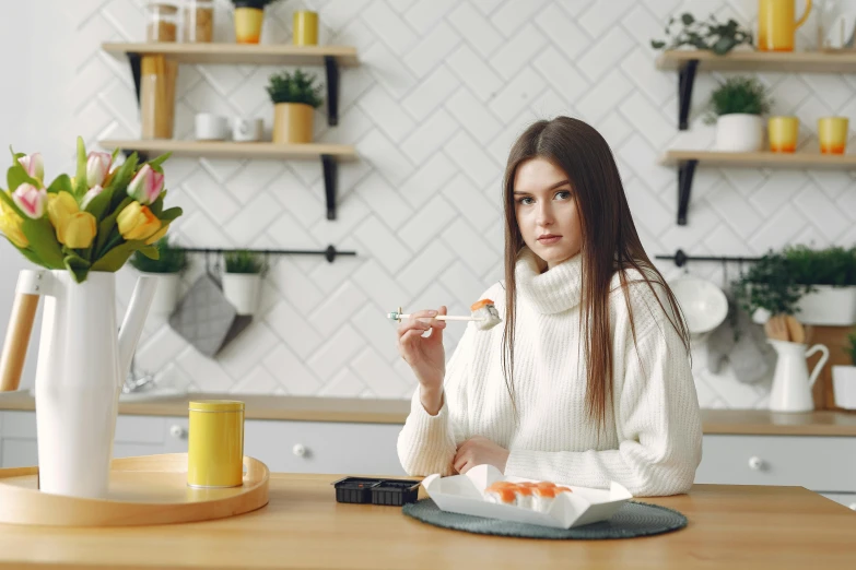 a woman sitting at a table with a plate of food, orange and white, ready to model, eating sushi, wearing casual sweater