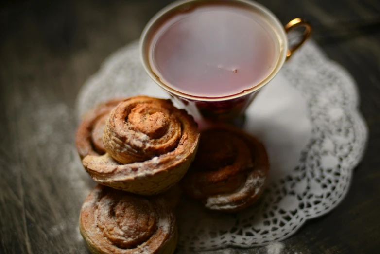 a cup of tea and some pastries on a doily, by Emma Andijewska, pexels contest winner, twinkling and spiral nubela, piled around, rose twining, 6 pack