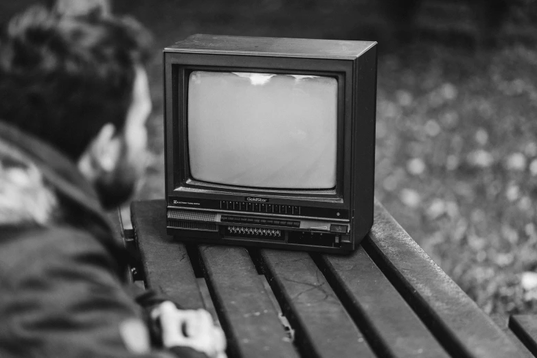 a small television sitting on top of a wooden bench, a black and white photo, by Felix-Kelly, pixabay, video art, sad man, 1 9 8 0 s tech, instagram post, advert